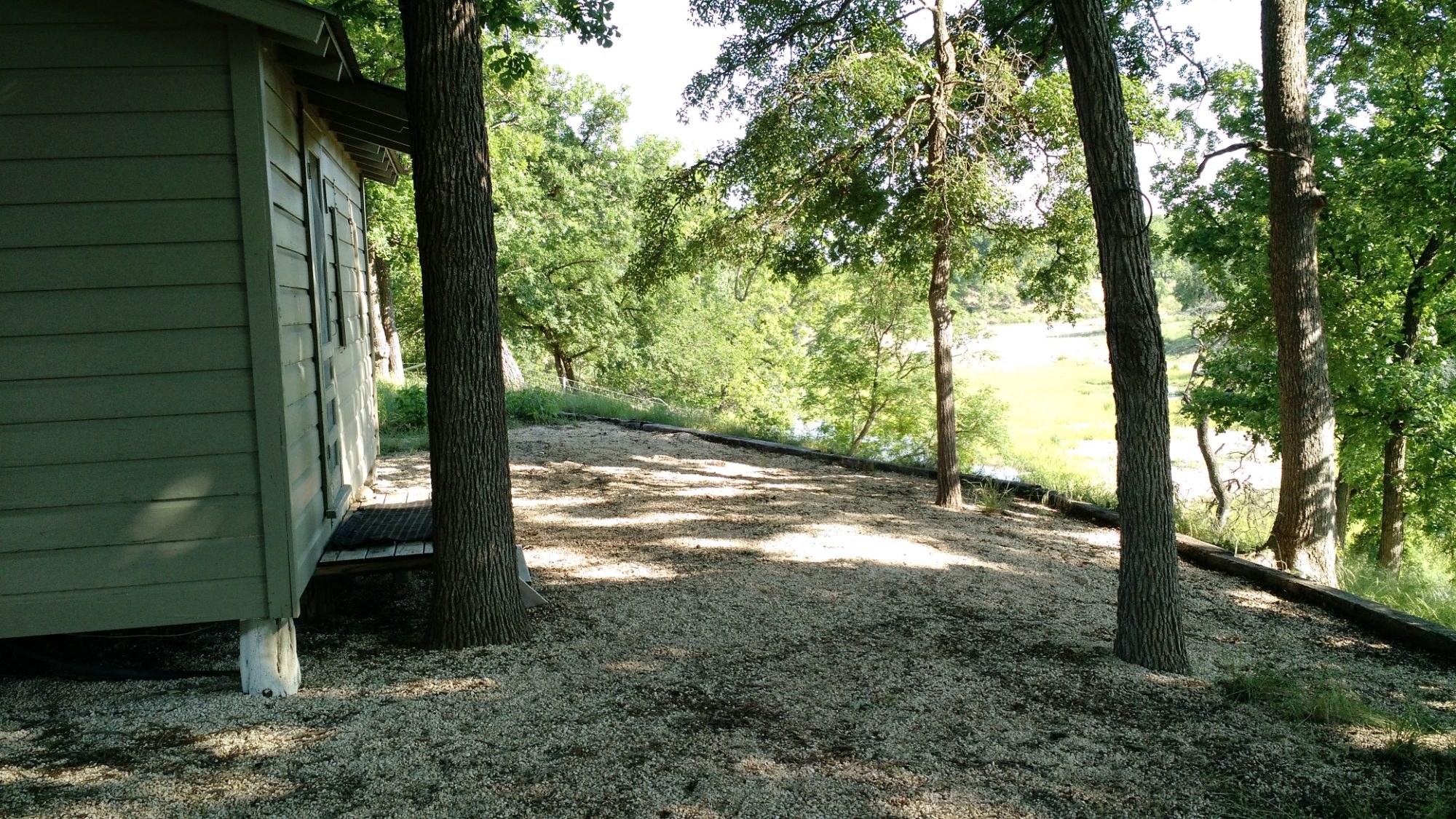 The cabin above the Lampasas River, gravel yard and oaks, river visible beyond